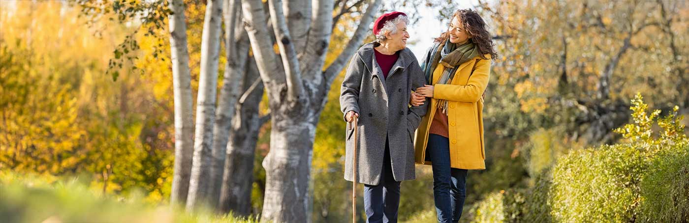 An older woman and a younger woman enjoy a walk down an outdoor nature trail in the Fall