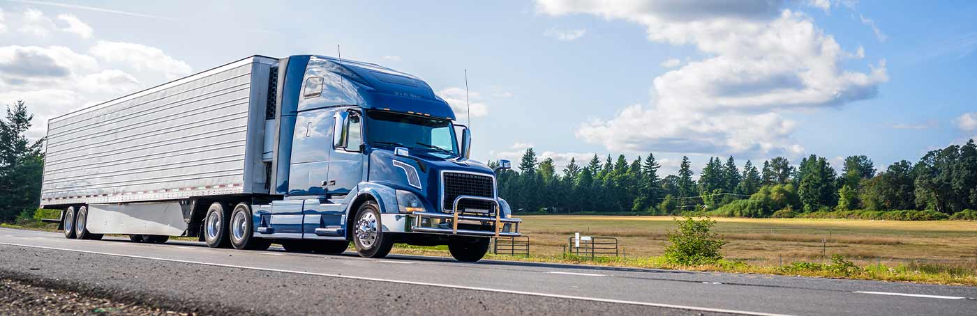 A blue big rig semit-truck driving on a rural road