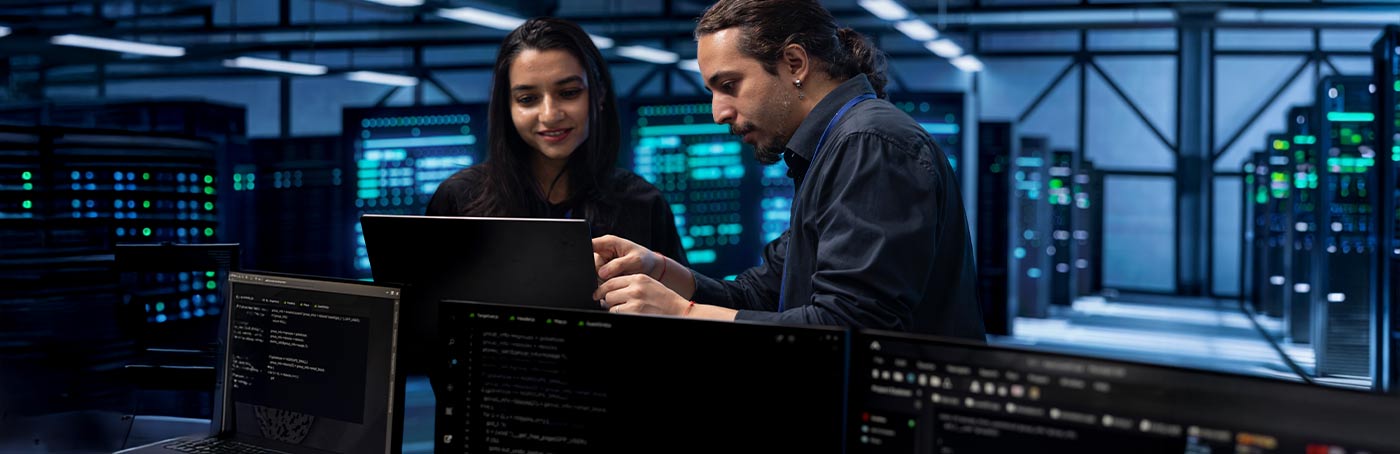 A man and a woman look at a laptop, working inside of a data center