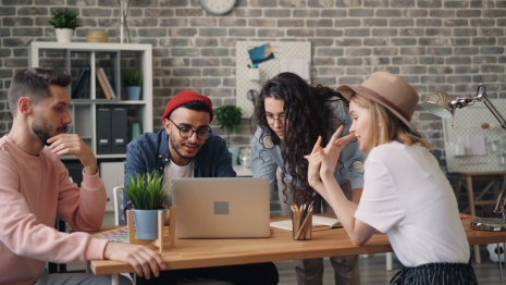 group of young adults gathered around a laptop discussing work plans